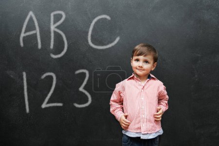 Photo for Child, boy and face with smile by blackboard with letters, numbers and happiness in classroom at school. Kid, student and happy for knowledge, learning and chalkboard with math, alphabet or preschool. - Royalty Free Image