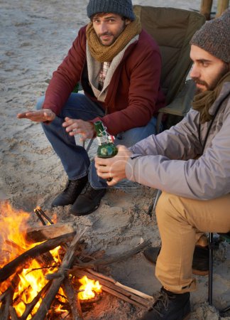 Photo for Men, sunset and campfire with portrait, smile and beer with travel adventure and journey outdoor. Friends, ocean and sea with bonding, winter and vacation by the beach together on holiday with fire. - Royalty Free Image