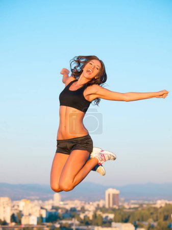 Photo for Woman, exercise and jump to air of sky in city of buildings on the roof with mouth open in happiness. Person, workout and fitness for health with energy for freedom of sports, wellness and athletic. - Royalty Free Image