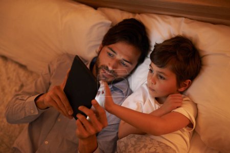 Photo for Bedroom, father and son with tablet, evening and family with ebook and connection with social media. Dad, home and boy with tech or bedtime with lights or bonding together with hobby or storytelling. - Royalty Free Image