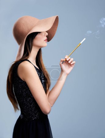 Foto de Glamour, perfil y mujer en sombrero con cigarrillo, confianza y moda vintage en estudio. Estilo clásico, chic y elegante con chica fumando sobre fondo gris en ropa de diseño con estética - Imagen libre de derechos