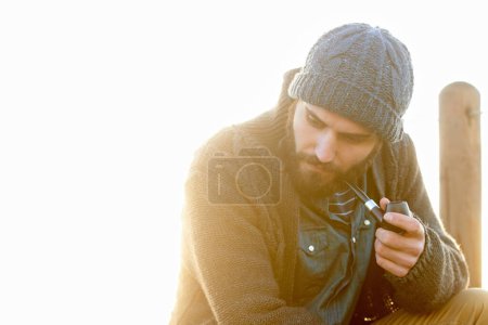 Photo for Young, man and smoking a pipe in outdoor, thinking and tobacco habit in morning by sunrise. English guy, nicotine addiction and retro smoker for calm, satisfaction and vacation by ocean in cape town. - Royalty Free Image