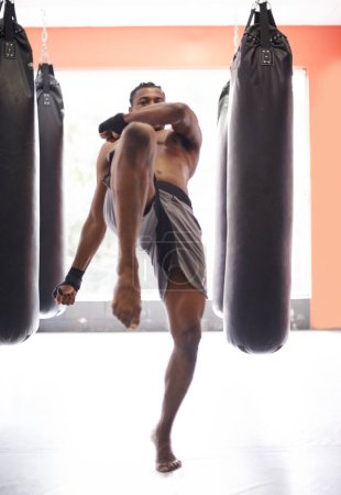 Téléchargez les photos : Homme, kick boxing et sac avec entraînement, genou et combat pour l'exercice avec équilibre, puissance et précision dans la salle de gym. Athlète, personne ou combattant africain avec entraînement, remise en forme ou frappe pour le défi dans le dojo. - en image libre de droit
