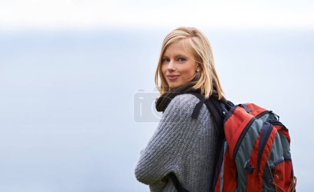 Photo for Woman, hiking and portrait for travel, adventure and wellness on a cloudy sky or grey background in winter. Face of a young person in backpack for trekking, explore or journey outdoor with mockup. - Royalty Free Image