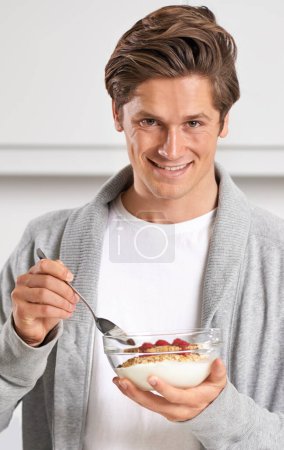 Foto de Sonrisa, retrato y hombre con cereal en cocina de hogar para hidratación, salud y bienestar. Hombre feliz, seguro y joven desayunando con fruta, yogur y muesli en un apartamento moderno - Imagen libre de derechos