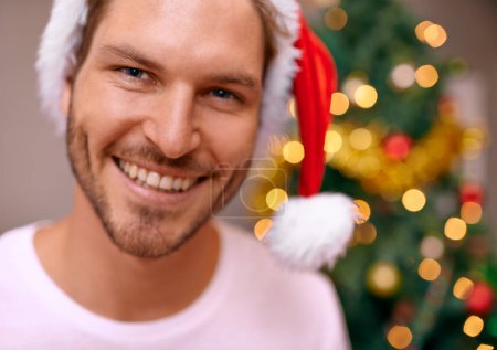 Foto de Hombre, sombrero de fiesta y retrato junto al árbol de Navidad, celebración y sonrisa en casa en vacaciones religiosas. Hombre, feliz y especial decoración para vacaciones festivas, tradición y alegre para el evento. - Imagen libre de derechos