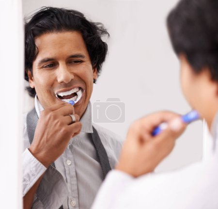 Téléchargez les photos : Dentaire, miroir et homme se brossant les dents dans une maison pour l'hygiène, la beauté ou la routine du matin avant le travail. Blanchiment des dents, bouche et homme d'affaires avec brosse à dents dans la salle de bain pour dents, nettoyage ou bien-être. - en image libre de droit
