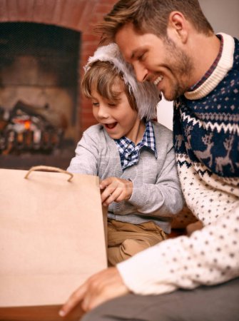 Photo for Father, son and opening gift on Christmas, curiosity and happy for celebrating a festive holiday. Daddy, child and bonding on religious vacation in living room, childhood and tradition of present. - Royalty Free Image