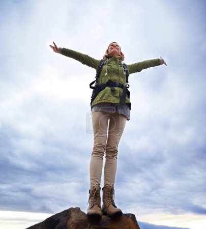 Photo for Woman, hiking and freedom on mountain top for travel, success and achievement or fresh air on cloudy sky. Young person in backpack and stretching arms for trekking, journey or adventure in low angle. - Royalty Free Image
