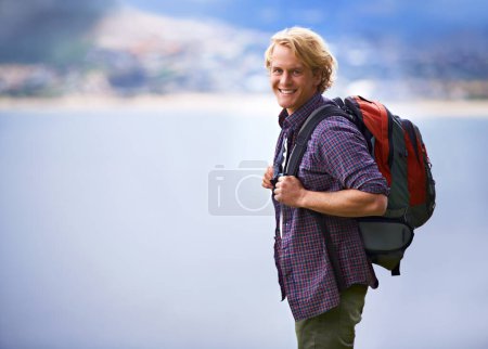 Photo for Man, hiking and portrait in nature for travel, adventure and wellness by ocean, sea and vacation in Europe. Face of an happy and young person with backpack for trekking, explore and outdoor journey. - Royalty Free Image