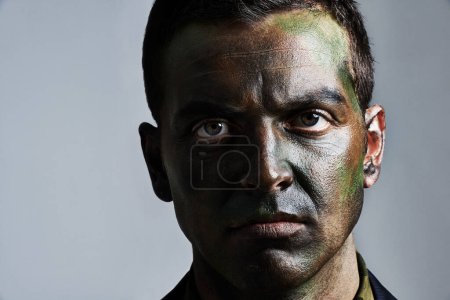 Photo for Man, portrait and camouflage with face paint for war, battle or military service on a gray studio background. Closeup of male person, army or solider with color dye for undercover disguise on mockup. - Royalty Free Image