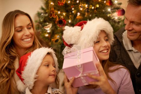 Foto de Navidad, padres e hijos con caja de regalo en el árbol para la celebración emocionada, feliz y sorpresa juntos. Vacaciones, festivo y mamá, papá y los niños en el sofá para dar regalos, Navidad y amor en casa - Imagen libre de derechos