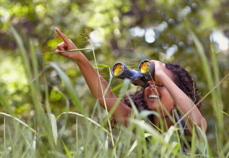 Photo for Nature, binoculars and girl in grass for exploring in park on vacation, adventure or holiday. Travel, forest and young child or kid with equipment in lawn in outdoor field or woods on weekend trip - Royalty Free Image