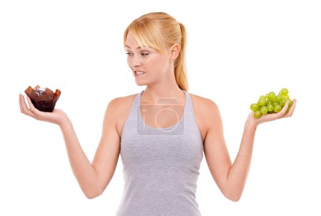 Photo for Portrait, confused and woman with choice of fruit, cake or healthy food to lose weight in studio. Decision, face and girl with grapes vs chocolate dessert for diet, nutrition and white background - Royalty Free Image