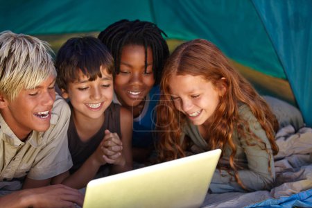 Photo for Laptop, happy and children in tent for camp watching movie, film or show online together. Smile, technology and young kids bonding, relax and streaming video on internet with laptop on weekend trip - Royalty Free Image