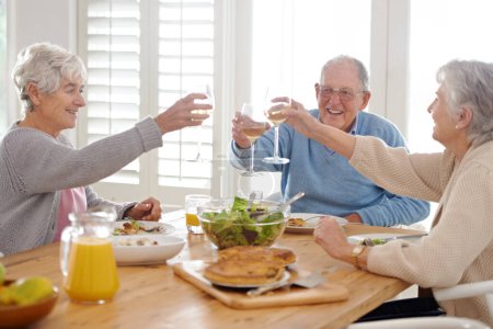 Foto de Vino, vítores y amigos mayores en el almuerzo en casa con sonrisa, celebración y vinculación en la jubilación. Comida, bebidas y tostadas con vidrio, anciano y mujeres en la mesa juntos para el brunch feliz - Imagen libre de derechos