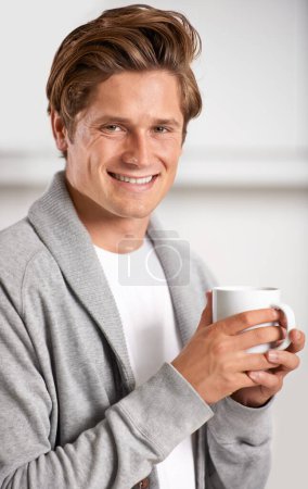 Téléchargez les photos : Sourire, portrait et homme avec tasse de café dans la cuisine de la maison pour se détendre, la santé et le bien-être. Heureux, confiant et jeune homme buvant cappuccino, expresso ou latte dans un appartement moderne - en image libre de droit