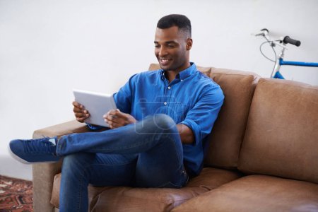 Photo for Man, tablet and relax on social media at home, online and internet for website or blog. Black male person, smile and streaming entertainment on armchair, video call and app for shopping on weekend. - Royalty Free Image