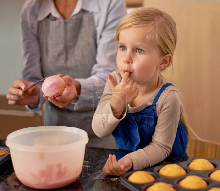 Photo for Child, baking and eating icing in kitchen for cupcake decoration or hungry for sweet snack, helping or ingredients. Teamwork, girl and finger for recipe taste in home for youth bonding, food or fun. - Royalty Free Image