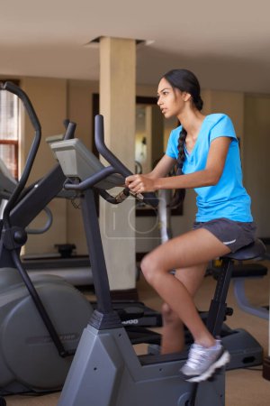 Woman, cardio and exercise bike in gym, active and stationary machine for workout at club. Female person, body health and cycling for strength training, challenge and equipment for fitness or action.
