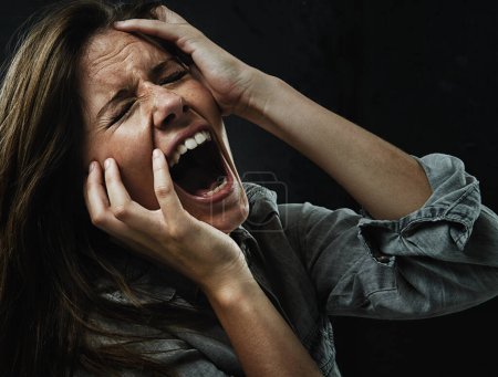 Photo for Face, stress and horror with woman yelling in studio on black background for reaction to fear. Phobia, mental health and breakdown with scared young person in dark for drama, nightmare or terror. - Royalty Free Image