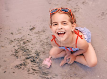 Téléchargez les photos : Happy, portrait et petite fille jouant avec le sable à la plage pour des vacances amusantes, week-end ou été. Visage de femme, enfant ou enfant avec le sourire dans le bonheur pour la journée par le rivage sablonneux dans la nature. - en image libre de droit