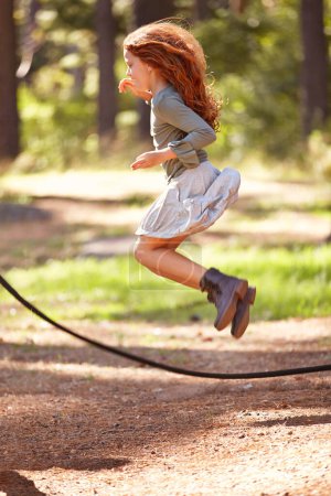 Photo for Jump, rope and girl outdoor for game in forest, park or playing on summer, holiday and vacation. Child, skipping and energy for fun activity in nature with trees in backyard or garden with kid in air. - Royalty Free Image