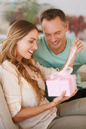 Woman opening gift, man and happy with surprise for birthday or anniversary, love and support with romance. Couple in marriage, unboxing package with ribbon and present for token of appreciation.
