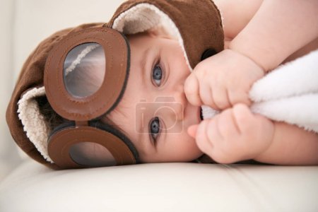 Photo for Baby, portrait and pilot hat or happy at home on bed for childhood development for growth, blanket or comfortable. Kid, boy and face airplane flying accessory in apartment for peace, relaxing or rest. - Royalty Free Image