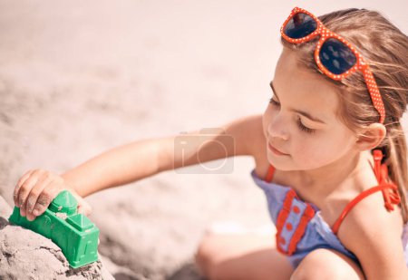 Téléchargez les photos : Fille, jouets et bâtiment château de sable sur la plage avec forme ou bloc pour le plaisir d'été, vacances ou week-end dans la nature. Femme, enfant ou enfant jouant et appréciant la construction de sable au bord de l'océan. - en image libre de droit