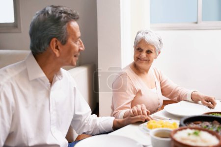 Téléchargez les photos : Couple de personnes âgées, dîner et se tenir la main dans la salle à manger à la maison, prier et gratitude pour le repas. Grace, sourire et amour lors du déjeuner d'action de grâce, les retraités et les personnes âgées profitent du temps en famille en Amérique. - en image libre de droit