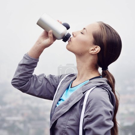 Foto de Mujer, bebida y botella de agua para fitness, desintoxicación y bienestar en el día nublado en Francia con maqueta. Mujer sedienta, ropa deportiva e hidratada con ejercicio, entrenamiento y entrenamiento para la salud. - Imagen libre de derechos