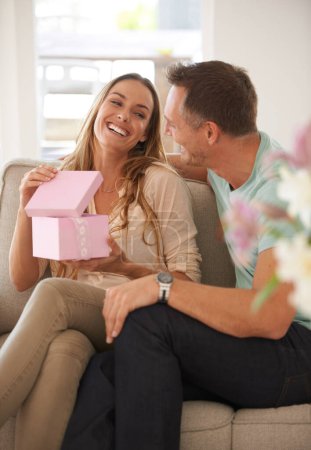 Happy woman opening present, man and smile with surprise for birthday or anniversary, love and support with romance. Couple in marriage, unboxing package and gift giving for token of appreciation.