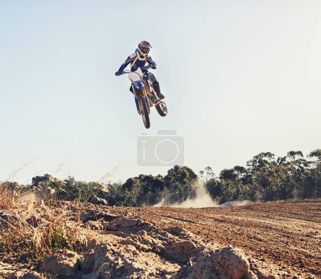 Person, jump and motorbike of professional motorcyclist in the air for trick, stunt or race on outdoor dirt track. Expert rider on bike or scrambler in dunes or extreme sport with blue sky background.