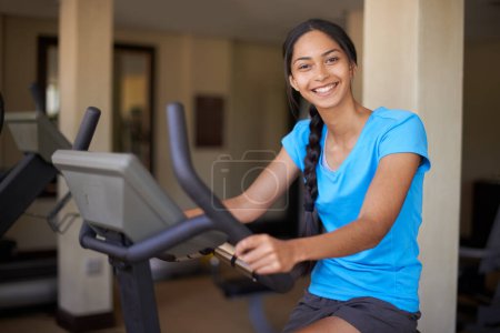 Photo for Woman, portrait and exercise bike in gym, cycling and stationary machine for workout at club. Female person, cardio and cycling for strength training, smile and equipment for fitness and health. - Royalty Free Image