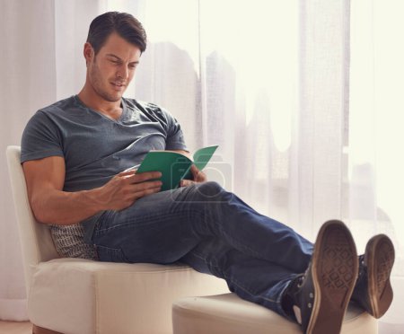 Photo for Man, relax or reading with book on chair in living room for story, literature or novel at home. Handsome male person or young adult for information, knowledge or learning in leisure or break at house. - Royalty Free Image