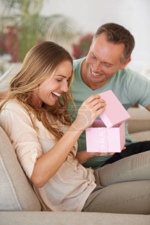 Woman opening present, man and happiness with surprise for birthday or anniversary, love and support with romance. Couple in marriage, unboxing package and gift giving for token of appreciation.