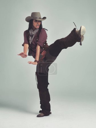 Photo for Western, woman and cowboy in studio with fashion, leg up and gesture to fight on grey background. Female person, vintage and outlaw with boots for wild west, costume and character with retro hat. - Royalty Free Image