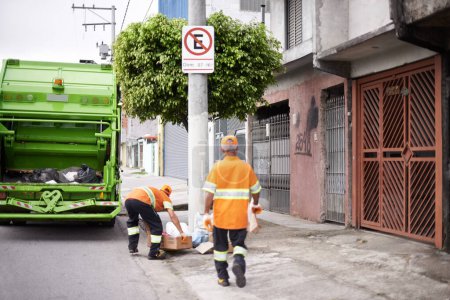Foto de Hombres, camión de basura y servicio de recogida en la ciudad para el medio ambiente público con trabajo en equipo, reciclaje o gestión de residuos. Uniforme, mantenimiento y transporte de suciedad en Nueva York, saneamiento o basura. - Imagen libre de derechos