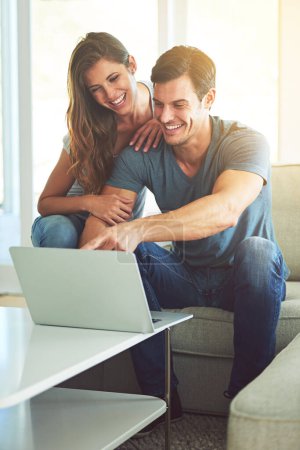 Photo for Couple, home and sofa with laptop, pointing and entertainment in living room with smile and laugh. Man, woman and couch with embrace, relax and love while bonding at tech in lounge at house. - Royalty Free Image