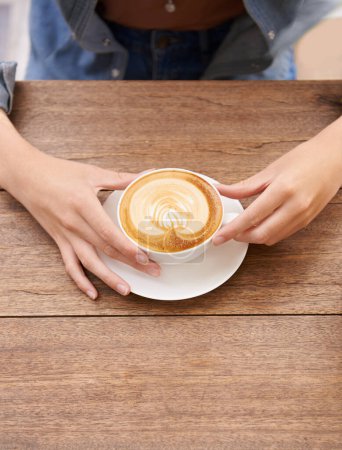 Foto de Manos de persona, taza de café y espuma en café expreso, cafeína y latte arte en mesa de madera. Taza de capuchino, leche caliente y crema para el gusto con bebida, bebida fresca y caliente en el restaurante para el descanso. - Imagen libre de derechos