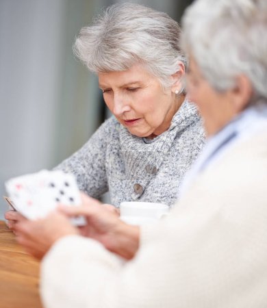 Foto de Las mujeres mayores, pensando y jugando a las cartas con el juego para los amigos en la jubilación, relajarse y unirse. Personas mayores, póquer y estrategia con seria diversión en la mesa en el hogar de ancianos para el fin de semana - Imagen libre de derechos