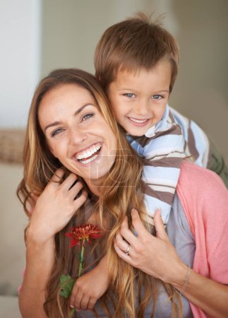 Téléchargez les photos : Portrait, mère et fils avec le sourire sur le dos pour la fête des mères, collage et ensemble à l'intérieur. Femme heureuse, garçon et rire avec la fleur, câlin et amour pour week-end ludique dans la maison familiale Nouvelle-Zélande. - en image libre de droit