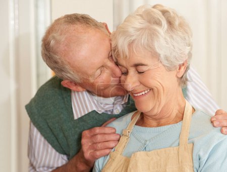 Téléchargez les photos : Couple sénior, romance et baiser à la maison, sourire et se lier ensemble à la retraite. Personnes âgées, amour et bonheur dans le mariage ou la relation, week-end et soutien dans l'engagement ou les soins dans la cuisine. - en image libre de droit