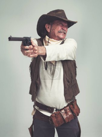 Foto de Vaquero, hombre mayor y pistola de tiro, arma o pistola en el estudio con traje aislado sobre un fondo blanco. Occidental, sheriff y persona madura con revólver, apuntando y asustado de miedo en Texas. - Imagen libre de derechos