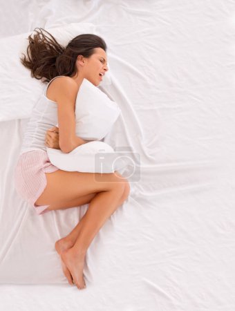 Photo for Woman, stomachache and pain on bed, cramps and appendicitis in home for discomfort. Female person, top view and constipation or ulcer in bedroom, muscle strain and bloating or menstrual crisis. - Royalty Free Image