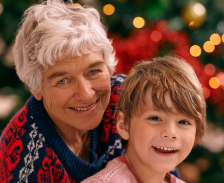 Foto de Navidad, retrato y celebración en salón, abuela y nieto sonríen con alegría. Casa, anciana y niño juntos para las vacaciones como familia en el salón, el árbol y el amor en el hogar. - Imagen libre de derechos
