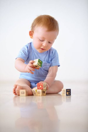Foto de Niño bebé, bloques de madera y jugar con juguetes en el desarrollo de la primera infancia en un fondo de estudio gris. Pequeño niño o niña en el suelo con forma o cubo en la construcción, el aprendizaje o las habilidades cognitivas. - Imagen libre de derechos
