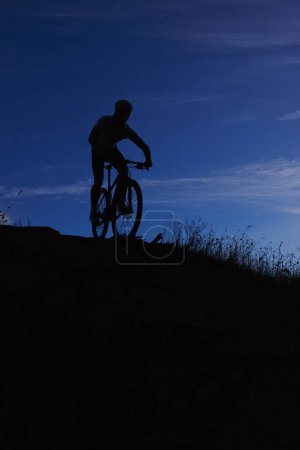 Téléchargez les photos : Cycliste, silhouette et balade à vélo la nuit, VTT et VTT à la campagne. Personne, liberté et maquette du ciel pour la remise en forme ou l'exercice, passe-temps et sports pour l'aventure en plein air et le cyclisme. - en image libre de droit