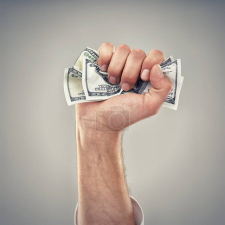 Photo for Closeup, hand and money for finance, greed and capitalism for business on grey background in studio. Fist, cash and dollar to invest, pay or loan for bid opportunity, trading and financial market. - Royalty Free Image